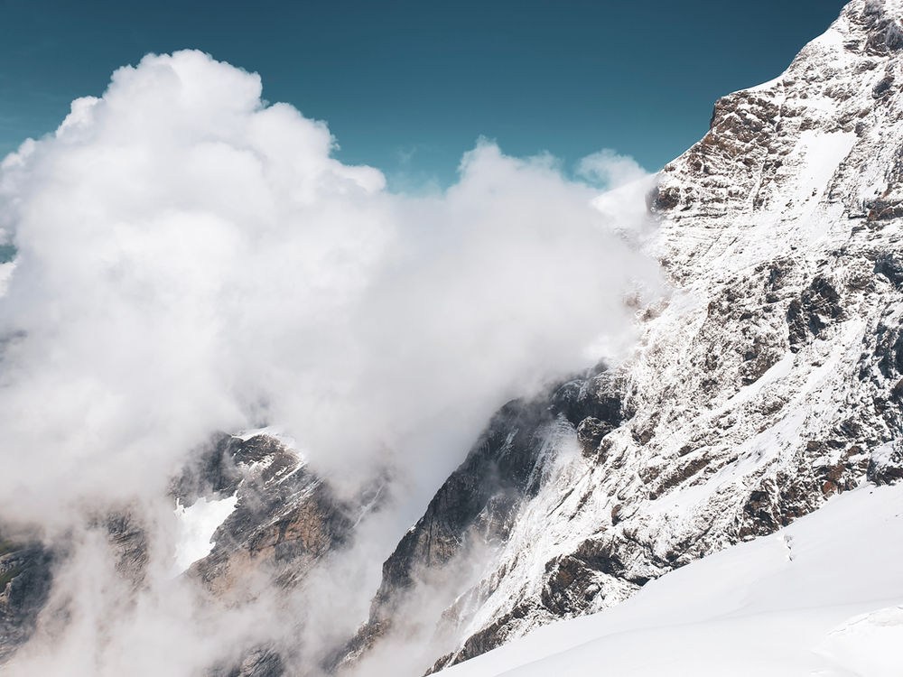 Snowy mountain peak surrounded by fluffy clouds under a clear blue sky. Rugged majesty and serene atmosphere dominate the scene. Depicts an avalanche to symbolize the debt avalanche method
